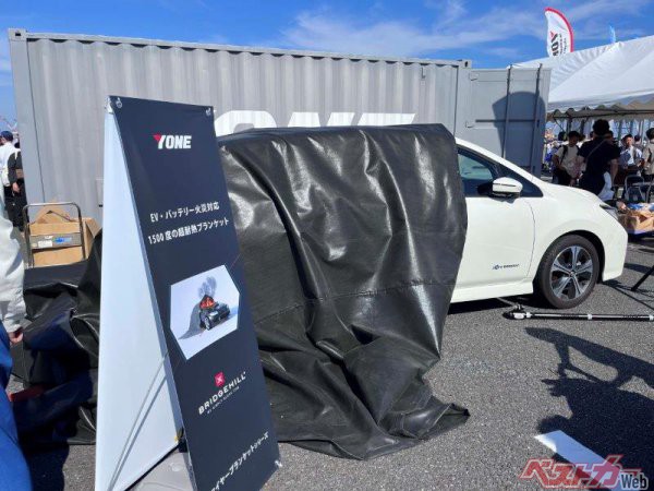 この写真は、EV・バッテリー火災対応1500度の超耐熱ブランケット。2023年6月行われた東京国際消防防災展で筆者が撮影。炎上中のEVにかけることで延焼を防ぐことができるという