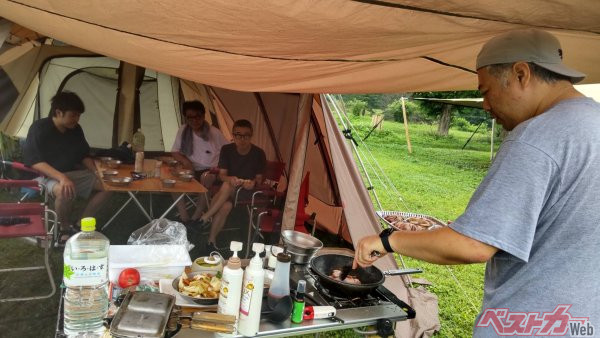 けだるい雰囲気のキャンプ翌朝に自ら食材を調理するWeb編集長の塩川。オイオイ、奥に座る3人の君たちは誰も手伝わないんかい！？