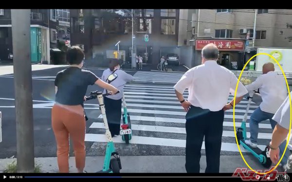 横断歩道を、電動キックボードに乗りながら渡ろうとする人