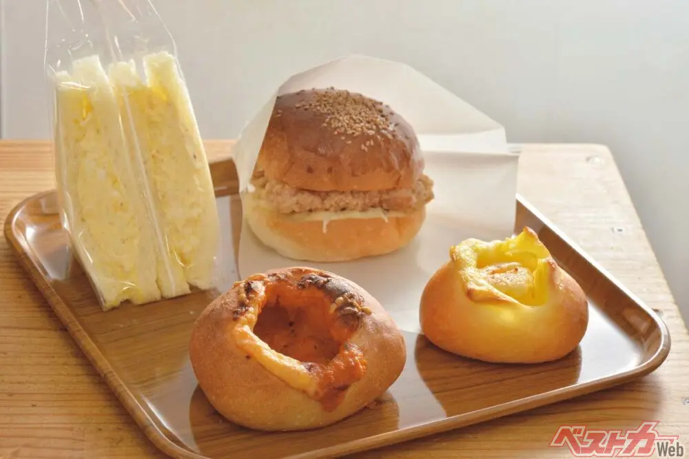 『手作り焼き立てパンの店 LISZT(リスト)』(左奥)たまごサンド 340円、(右奥)チキンタツタ 350円、(左手前)クリーミートマトチキン 250円、(右手前)マヨたく 195円 たくあんの甘みとマヨネーズの酸味がいい「マヨたく」。チキンとチーズがたっぷり入った「クリーミートマトチキン」。フィリングの味付けは塩・黒胡椒、マヨネーズとシンプルだからこそ素材の良さがわかる「たまごサンド」。周りをサクッと揚げたジューシーな鶏ムネ肉とワサビマヨが技ありの「チキンタツタ」