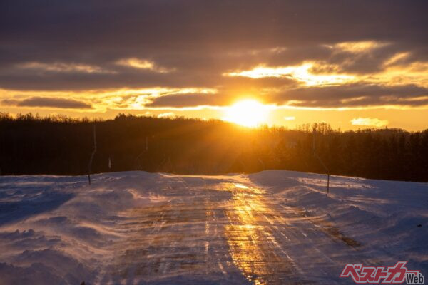 凍結して朝日を反射する夜明けの道路（satoshi tada@Adobe Stock）