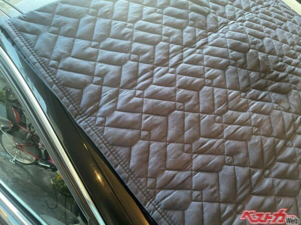 養生マットをフロントウインドウにかけておくだけで凍結を防ぐことができる。ただし飛ばされないように、左右のドアに挟まなければいけない