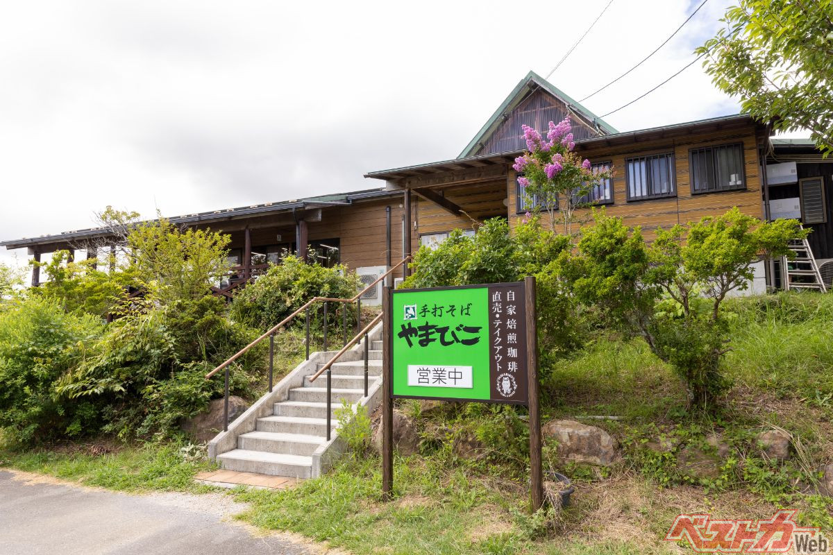 『手打そば　やまびこ』ロッジ風の外観。小高い山の頂上近くにあり、店内や駐車場からの眺望は抜群