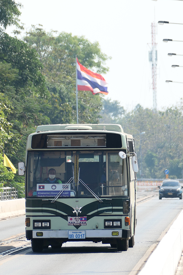 タイ国旗をバックに京都市営バスが国境の橋を渡る