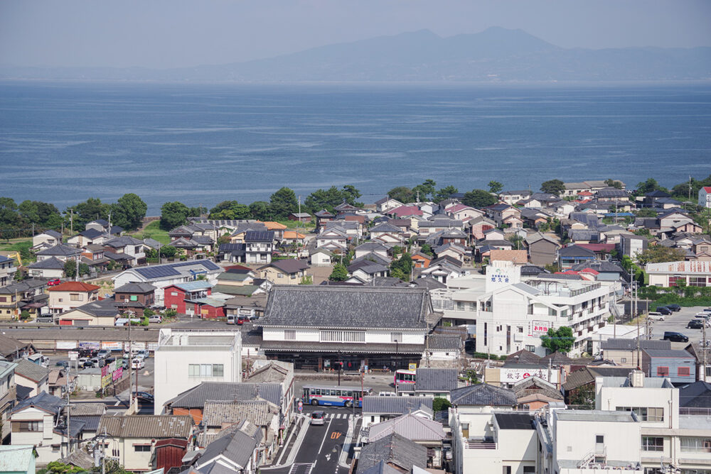 有明海を背景に島原の街が広がる天守からの眺め。正面に島原駅があり、貫禄のある駅舎は大手門をイメージしたデザイン