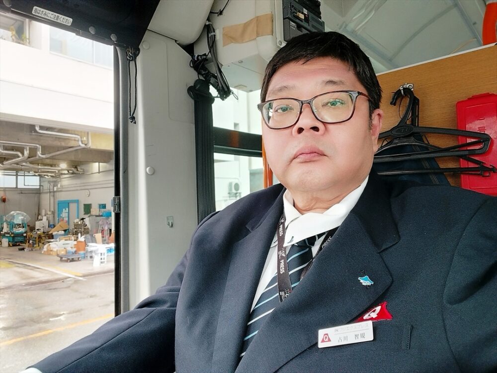 名札を付けた制服で運転席に座る