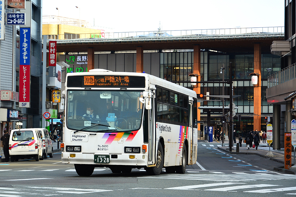 長野駅を出発し、中央通りを善光寺方面に右折する戸隠スキー場行きキュービック。背景の長野駅舎は長らく「仏閣型駅舎」として親しまれたが、新幹線開業を機に建て直され、2015年の北陸新幹線金沢開業を機にさらに一新された