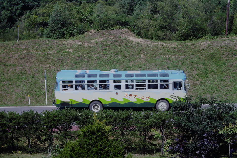 【写真1】北海道池田町の牧歌的風景の中を走る十勝バスの「ブルーグラス号」。過去の観光バスのシンボルだった天窓が鮮烈（1986年）