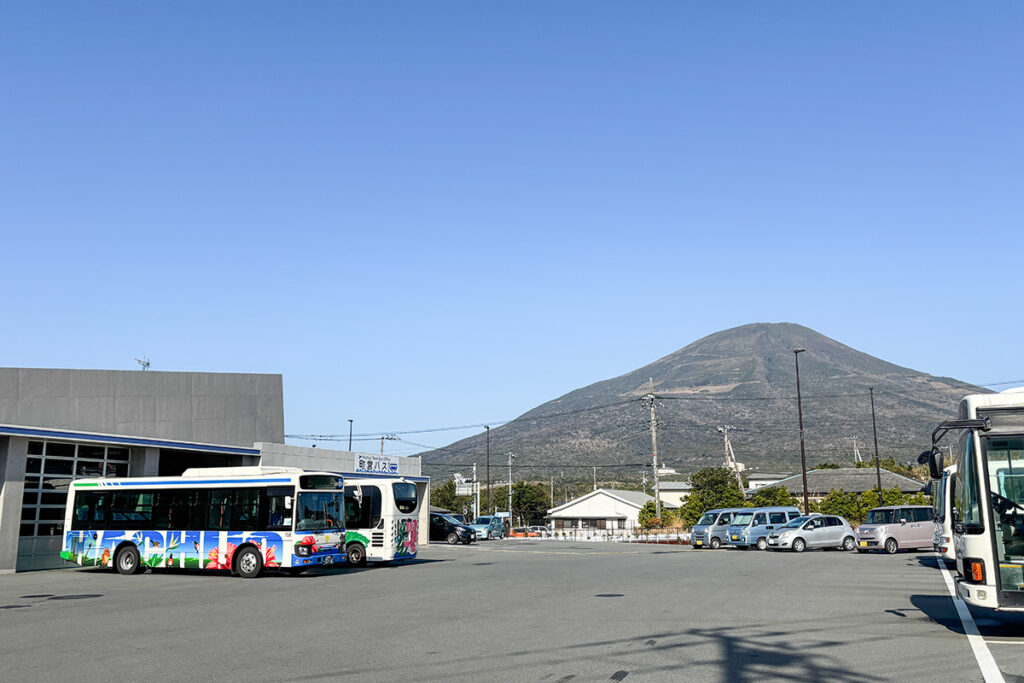 八丈島の町営バスが集まる「町営バス」バス停と車庫。奥には八丈富士が聳える