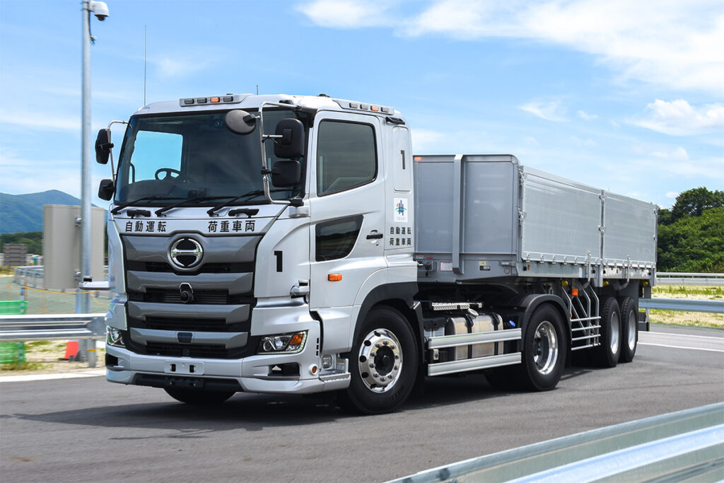 無人のままオーバル試験路からガレージへ帰庫する荷重車。ルーフには運行状態を車外に示すインジケータが設置されており、試験運行時(ブルー)とは異なるイエローが点滅している。同様のインジケータは、日野の他の自動運転実証車(港湾コンテナトレーラ)にも装備例がある