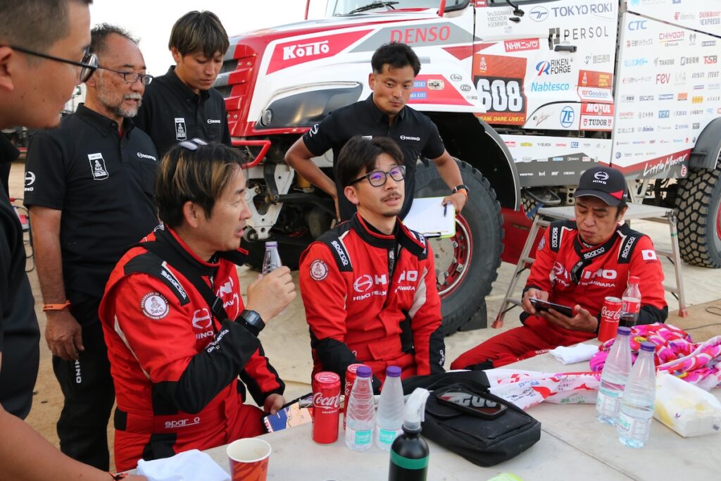 申し送りをする選手とメカニック。赤のレーシングスーツを身に纏った乗員メンバーは、左からナビゲーターの染宮弘和、メカニックの望月裕司、ドライバーの菅原照仁