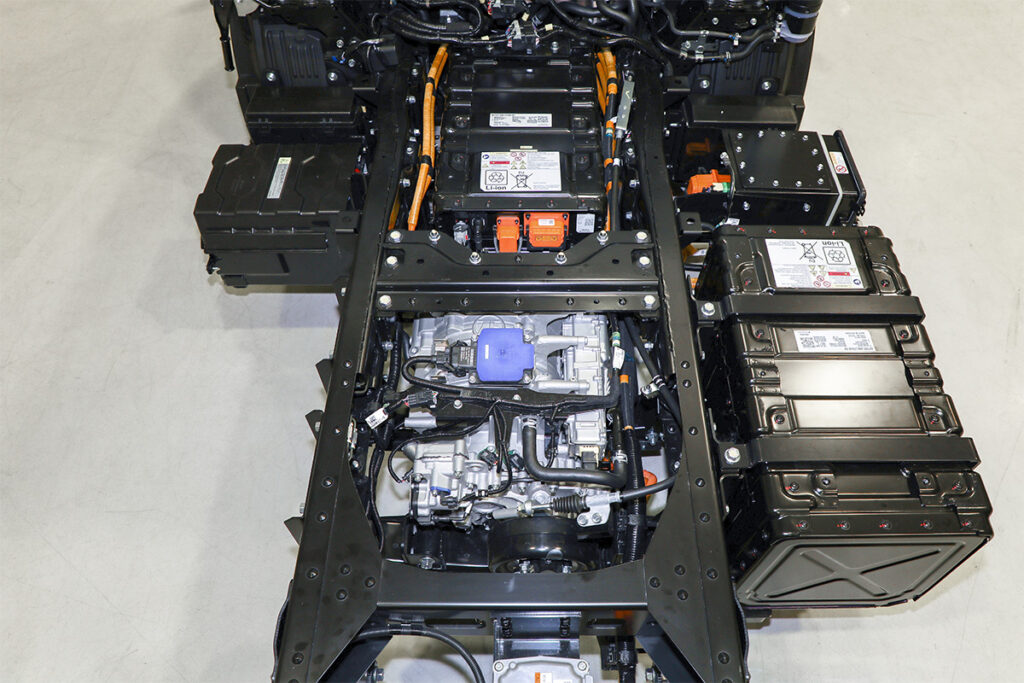 エルフEVのキャブ付シャシー。キャビン下に1／3ほど潜る形で高電圧バッテリーをまず1基搭載（シャシーフレームの間）し、フレームサイドにも1基または2基あるいは4基を搭載する（写真は計2基仕様）。量産FCトラックではどのような配置を採用するだろうか？