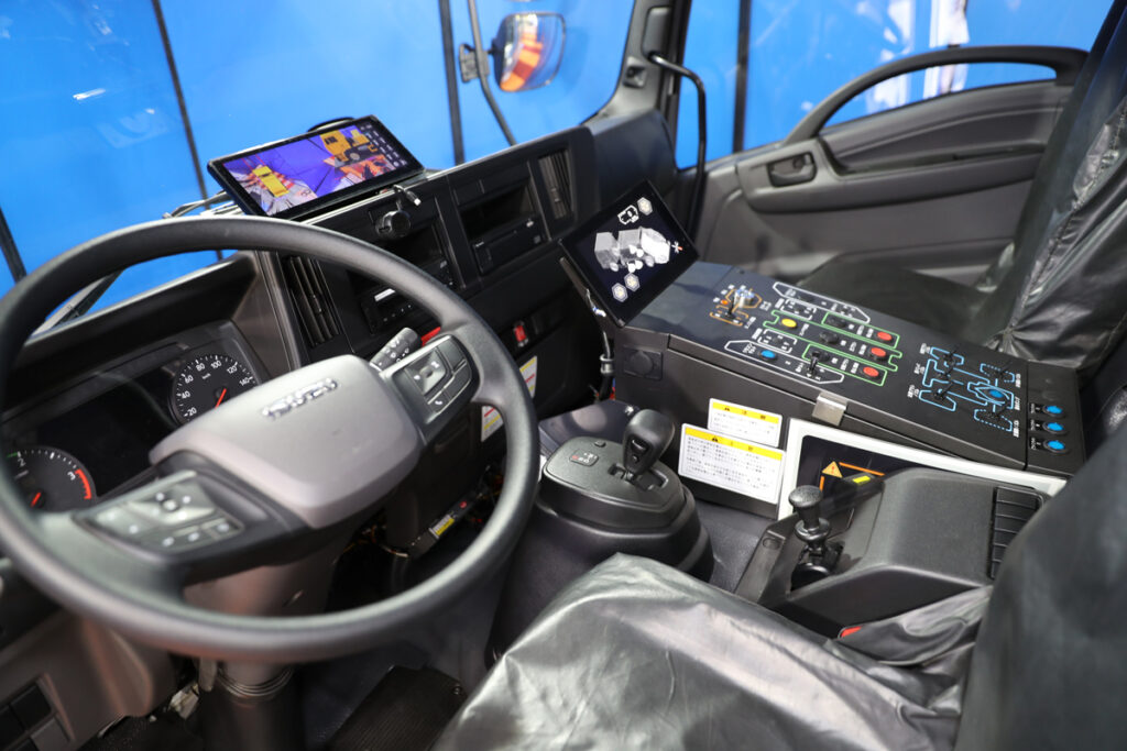 路肩が見やすい左ハンドル仕様の運転席。新型は作業専用モニターが追加装備され、コントロールボックスのデザインも一新されている